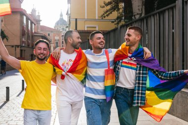 Sıcak gün batımı ışığında yıkanan dört eşcinsel arkadaş, güneşli bir şehirde LGBTQ bayrakları, çantalar, gömlekler ve daha fazlası ile süslenmiş bir şekilde dolaşırken sıkı bir kucaklaşmayı paylaşıyorlar..