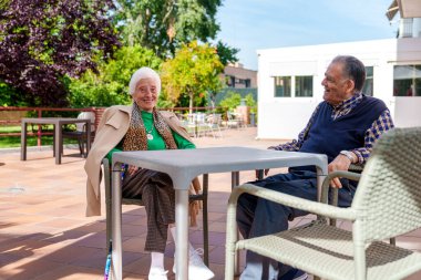 A delightful portrait captures the vibrant spirit of an elderly couple, radiating joy while seated in the geriatric home's picturesque patio surrounded by a beautiful garden. clipart