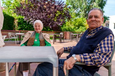 Neşeli yaşlı bir çift, güneşli bir günün sıcağında, huzur ve mutluluğu huzur içinde bir huzurevinin manzaralı bahçelerinde buluyorlar..