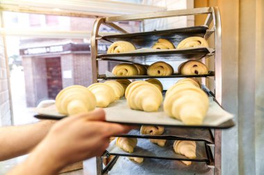 Anonim fırın işçisinin ellerinin yakın plan çekimleri titizlikle hazırlanmış tepsiler dolusu çikolatalı napolyon ve yeni pişmiş kruvasanları fırın için hazır hale getiriyor..