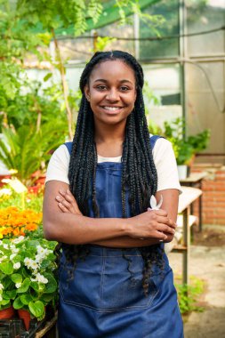 Işıldayan Afrikalı kadın, kolları çapraz, neşe saçan canlı, renkli bir botanik bahçesinde süs bitkileri ve çiçeklerle dolu.