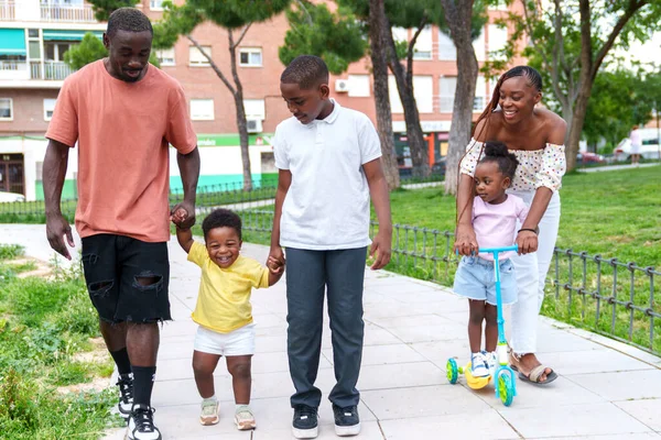 A vibrant, happy African family of five, with parents and three children, walk hand in hand through a colorful city park. Smiles and laughter fill the air as they embrace the joy of togetherness.