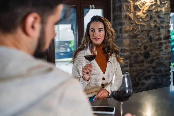 A young woman smiling with the couple with a glass of red wine on a romantic and happy evening in the kitchen of their home, lifestyle of a couple.