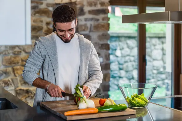 A young man preparing a salad in the kitchen of his rural home, lifestyle of a happy man.