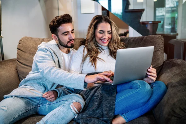 Close-up of a caucasian young couple in their living room watching TV while the wife is using the laptop computer. Lifestyle of a couple on a romantic evening. Domestic lifestyle.