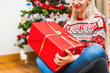 Şenlikli giyinmiş neşeli bir kadın. Kapalı alanda büyük bir Noel hediyesi sunuyor..