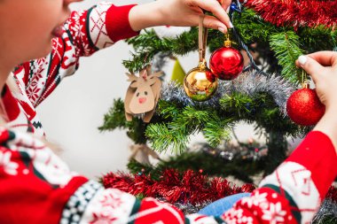 Noel ağacına ev yapımı ren geyiği dekoru ile şenlik süsleri asan ellerin yakın çekimi..