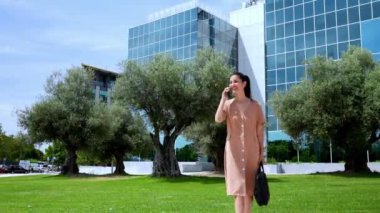 Zarif yönetici kadın, evrak çantasıyla lüks cam binaların arasında neşeli bir şekilde sohbet ediyor..