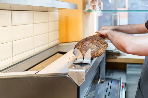 Professional baker slices a crusty artisan loaf with an industrial bread slicer in a clean bakery kitchen.