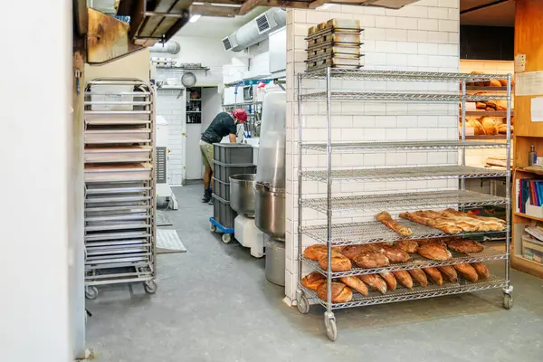 Commercial bakery scene with a baker working and shelves of fresh bread.
