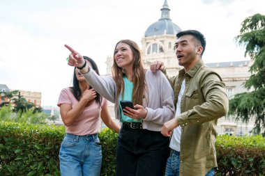 Asyalı erkek ve kadınların şehir parkında heyecan verici manzaraları gösterip paylaştıkları, gündelik kıyafet keşfi yapan genç üçlü..