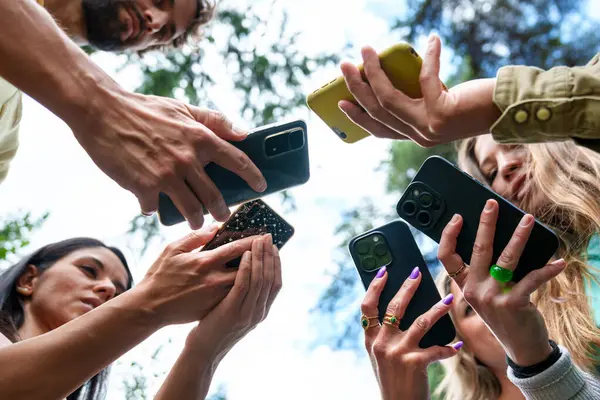 Bir park ortamında bir anı yakalamak veya paylaşmak için akıllı telefonları kullanan çeşitli bir grubun yakın plan görüntüsü