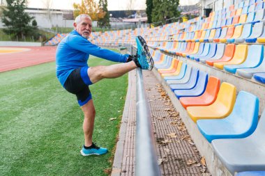 Atletik son sınıf öğrencisi sahada geriniyor. Arka planda hareketli boş tribünler, bulutlu bir gün.