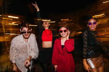 Neşeli bir grup arkadaş gece dışarıda parti yapıyor, moda ve eğlence gösterisi yapıyorlar..