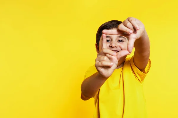 Young boy in yellow frames with fingers, playful gesture, matching vibrant background.
