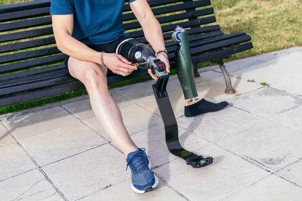 Unrecognizable active amputee adjusting a high-tech sports prosthetic leg in a park, embodying determination and athletic spirit.