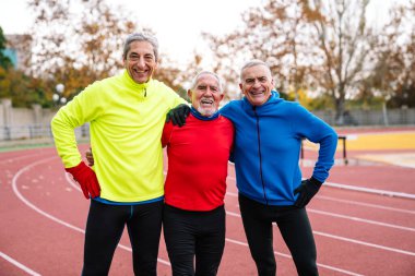 Renkli spor kıyafetleri içinde üç neşeli son sınıf öğrencisi atletik bir pistte birbirlerine bağlanıyor ve gülümsüyor, aktif bir yaşam tarzı sergiliyorlar..