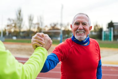 Kırmızılı neşeli kıdemli koşucu sahada el sıkışarak, aktif yaşam tarzı ve sportmenlik gösterisini kutluyor..