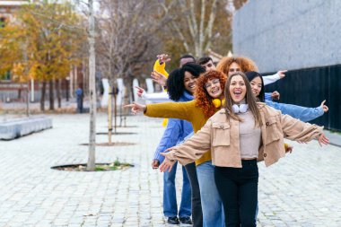 Bir kaldırım taşı caddesinde gülen ve poz veren bir grup genç arkadaş, kaygısız bir çok kültürlü kaynaşma anını yansıtıyorlar..