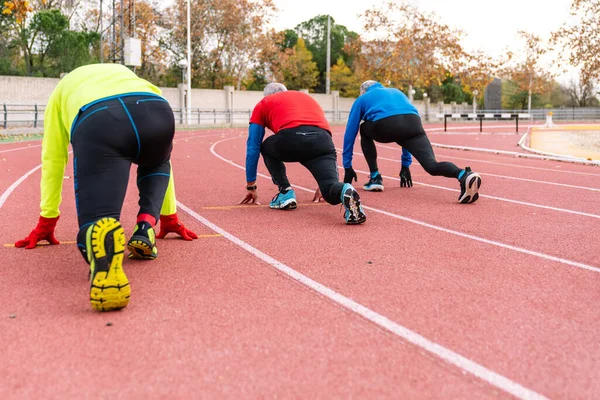 Elderly runners crouched at the start line in a stance of readiness, illustrating determination and active aging on a red running track.