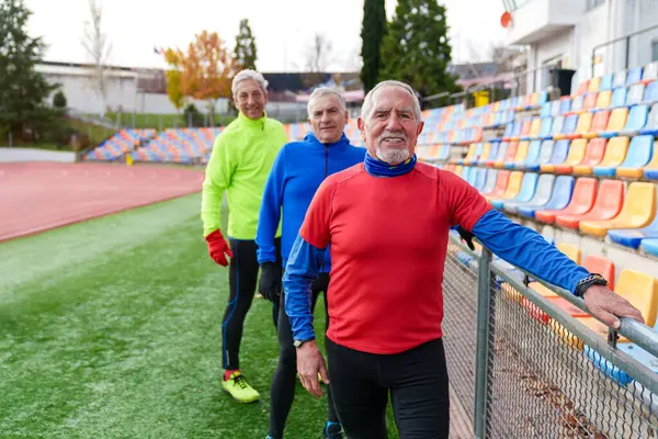 Three cheerful elderly male runners bonding and smiling on a colorful stadium track, promoting sports and health