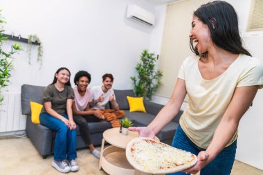 Mutlu kadın, hevesli arkadaşlarına ev yapımı bir pizza sunar. Kanepede dinlenir, sıcak, davetkar bir ev atmosferi yaratır.