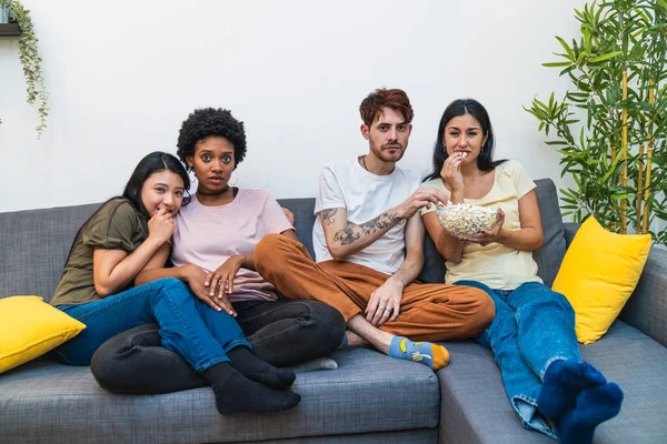 A diverse group of friends watching a movie at home, showing various reactions and enjoying their time together.