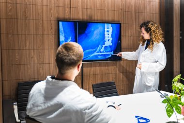 İki sağlık çalışanı, modern bir hastane ofisinde metal implantları olan bir ayak bileğinin ameliyat sonrası röntgenini analiz ediyor..