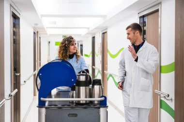 Kıvırcık saçlı hemşire tramvaydan hastane odalarına sıcak içecek servisi yapıyor, beyaz önlüklü, gülümseyen bir doktorla sohbet ediyor..