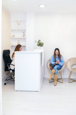 Modern, şık bir klinikte müşteriye danışmanlık yapan odaklanmış bir estetisyen. Hasta akıllı telefonuyla meşgul..