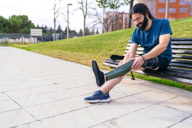 At kuyruklu sakallı sporcu karbon fiber protez bacağını bir bankta eğitime hazır hale getiriyor..