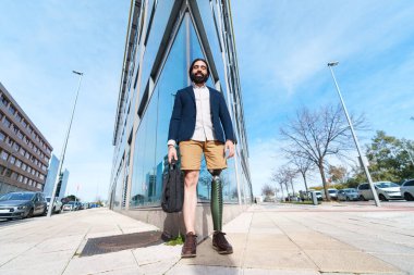 Protez bacaklı, kaldırımda yürüyen, şehir manzaralı, iş kıyafeti giymiş pozitif erkek girişimci..