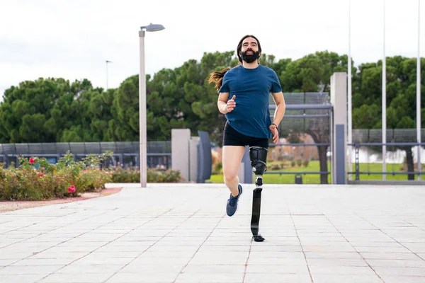 Frontal shot of a smiling bearded man with a state-of-the-art carbon fiber sports prosthetic leg, running in an urban park.