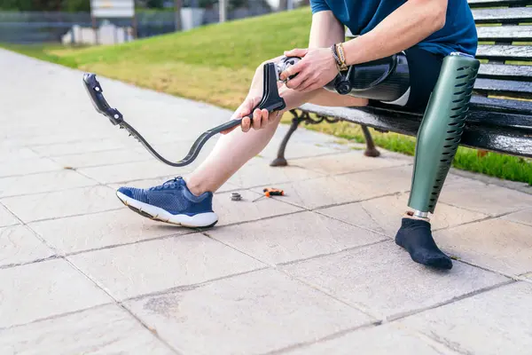 Athlete in sports gear tuning the foot of his carbon fiber prosthetic leg on a park bench, showcasing determination and independence.