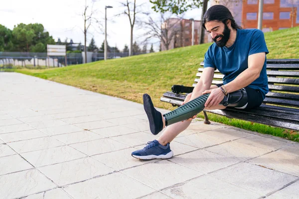 At kuyruklu sakallı sporcu karbon fiber protez bacağını bir bankta eğitime hazır hale getiriyor..