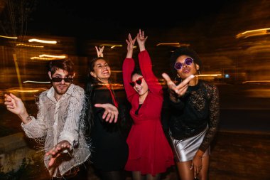 Neşeli arkadaşlar neşeli hareketlerle poz verirler, ışık tablosu birlikte geçirdikleri festival gecesi için canlı bir zemin oluşturur..