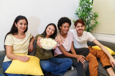Dört neşeli ev arkadaşı kanepede bir kase patlamış mısırla poz veriyor, evde rahat bir şekilde eğlenceli bir film gecesinin tadını çıkarıyorlar..