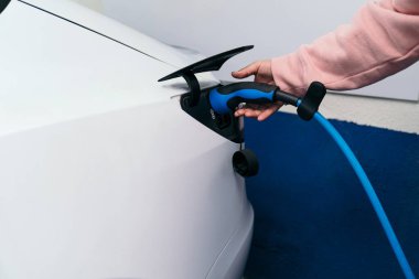 Tanımlanamayan pembe elbiseli biri mavi elektrikli araba şarjını beyaz bir araca bağlıyor..