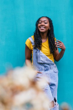 Kırmızı cep telefonuyla gülen, neşeli turkuaz bir arka planda duran neşeli, genç bir kadın..