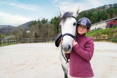 Gülümseyen at binen gözlüklü kız arenadaki benekli gri atıyla hassas bir anı paylaşıyor.