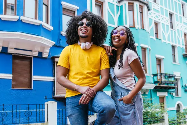 İki Latin arkadaş canlı bir şehir sahnesinde gülüyor ve kaynaşıyor, kültürel çeşitlilik ve neşe sergiliyorlar..