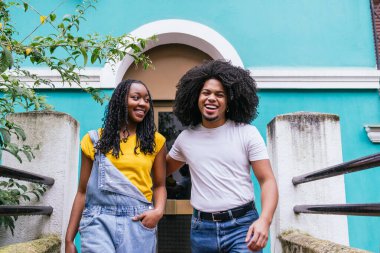 Birlikte gülen iki arkadaş, yemyeşil bir şehir ortamında neşeli bir anı paylaşıyor..