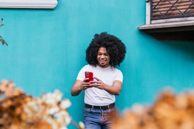 Parlak mavi duvarın önünde telefonu kullanan neşeli bir adam..