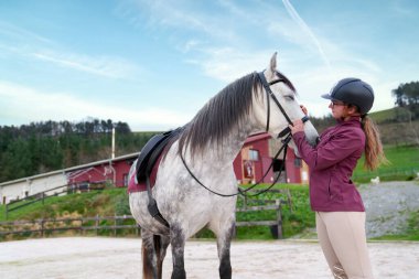 Kasklı bir sürücü beyaz atıyla dışarıda bir arenada..