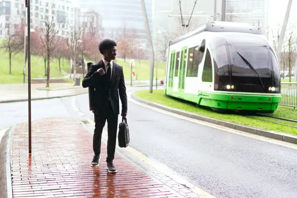A african businessman in a suit on a wet sidewalk by a tram.