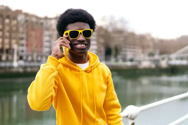 A happy African youth talking on a mobile phone by the river.