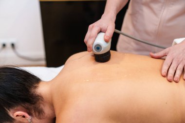 Bir fizyoterapist hastaya derin kas rehabilitasyonu için şok dalgası cihazı kullanır..