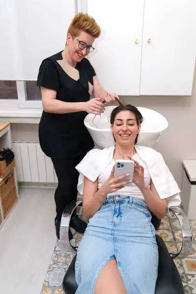髪の治療を受けている間の携帯電話の女性 — ストック写真