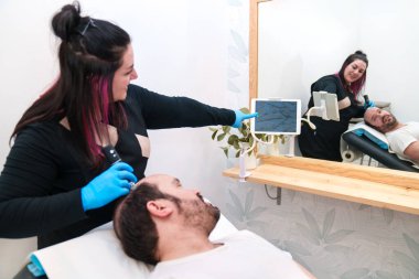 Teknisyen saç kaybı olan hastanın kafa derisini muayene ediyor..