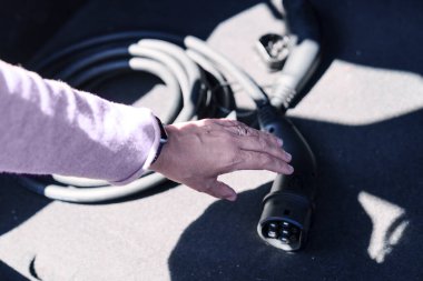 Bir el, sürdürülebilir güce bağlanmaya hazır bir EV şarj cihazını tutuyor..